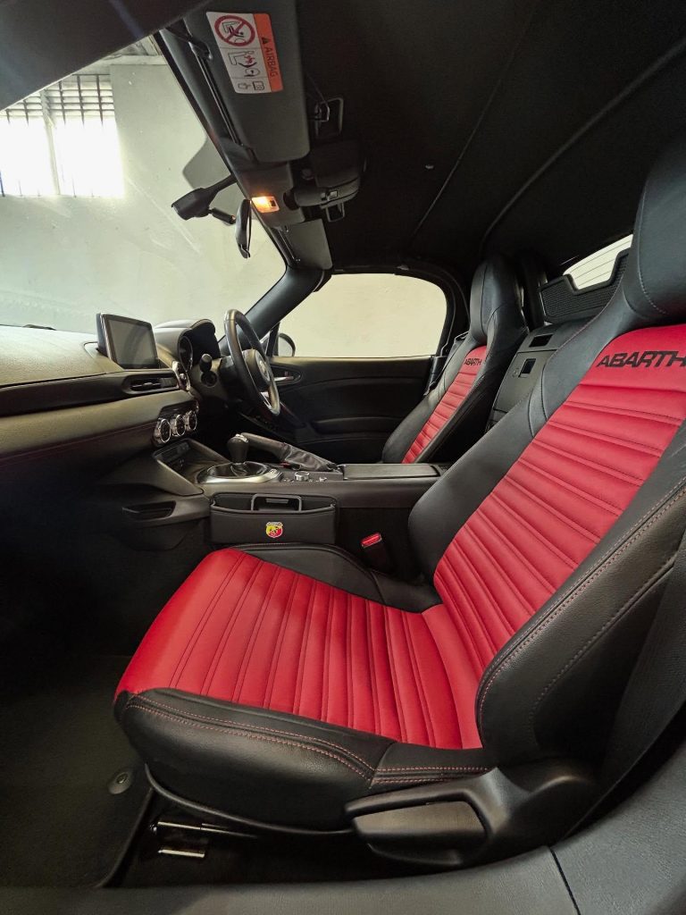 ### Key Elements  - **Main Subjects**: Car interior featuring sporty seats. - **Objects**: Dashboard, steering wheel, infotainment display. - **Notable Features**: Red and black leather seats with distinct stitching, modern design elements. - **Text/Symbols**: "ABARTH" logo on the seats, indicating the car's brand and sporty nature.  ### Overall Mood/Theme The image conveys a sense of luxury and sportiness, highlighting a modern and stylish car interior designed for performance enthusiasts. The color scheme suggests excitement and energy, enhancing the overall aesthetic appeal.